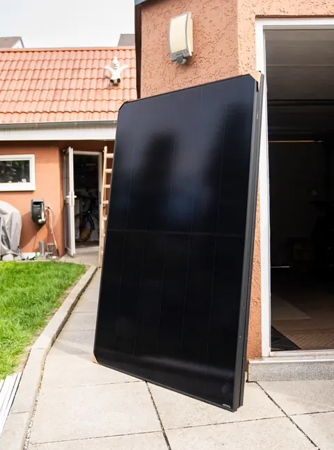 Ein schwarzes Solarmodul lehnt vor der Montage an einer Hauswand.
