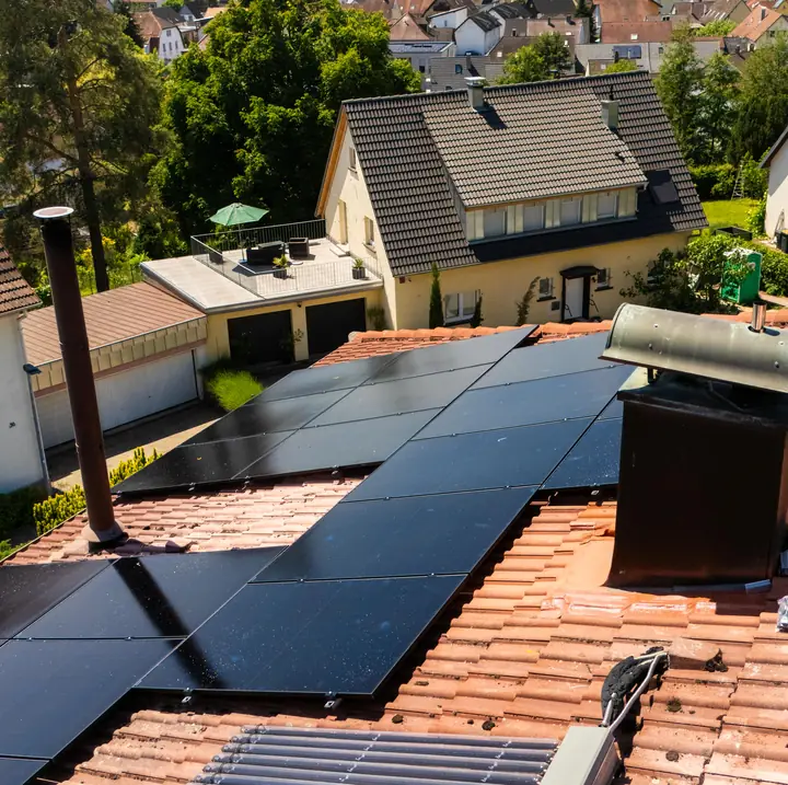 Fertige Solaranlage auf einem Ziegeldach, dahinter ein Ort mit Kirchturm und Feldern.