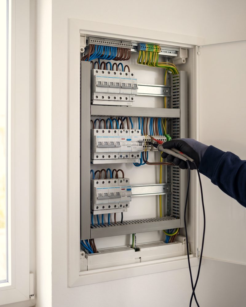 Ein Elektriker prüft mit einem Spannungsprüfer die Klemmen in einem ordentlich verdrahteten Zählerschrank.